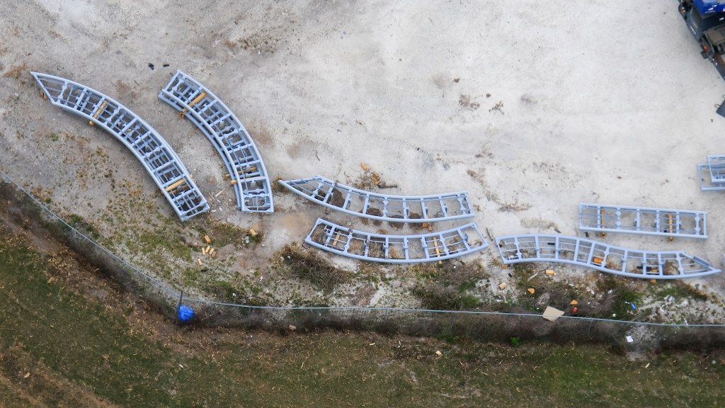 Aerial view of several curved metal frames arranged on a construction site, surrounded by dirt and grass.