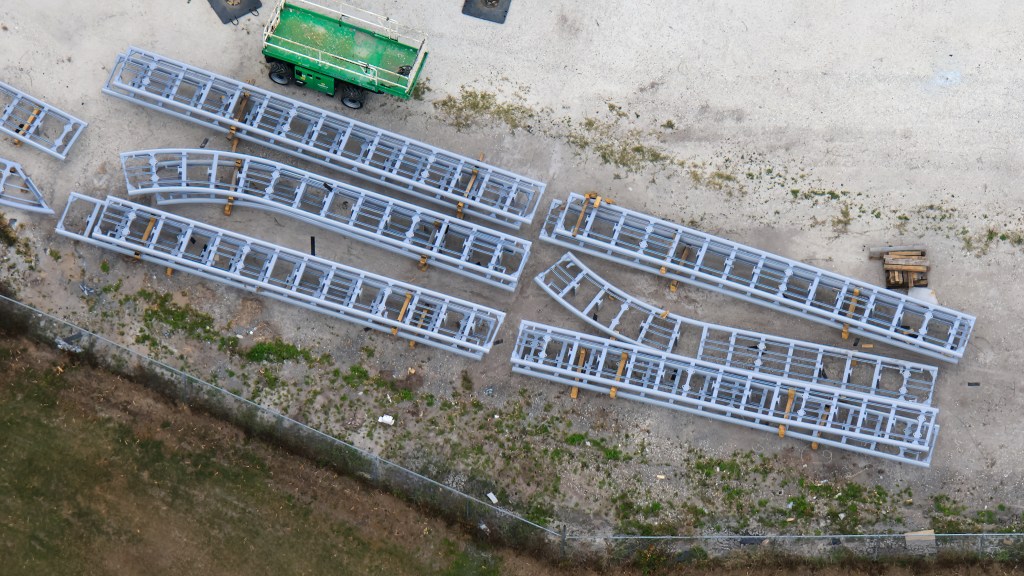 Aerial view of several large metal frameworks arranged on a gravel surface, with a green vehicle visible nearby.